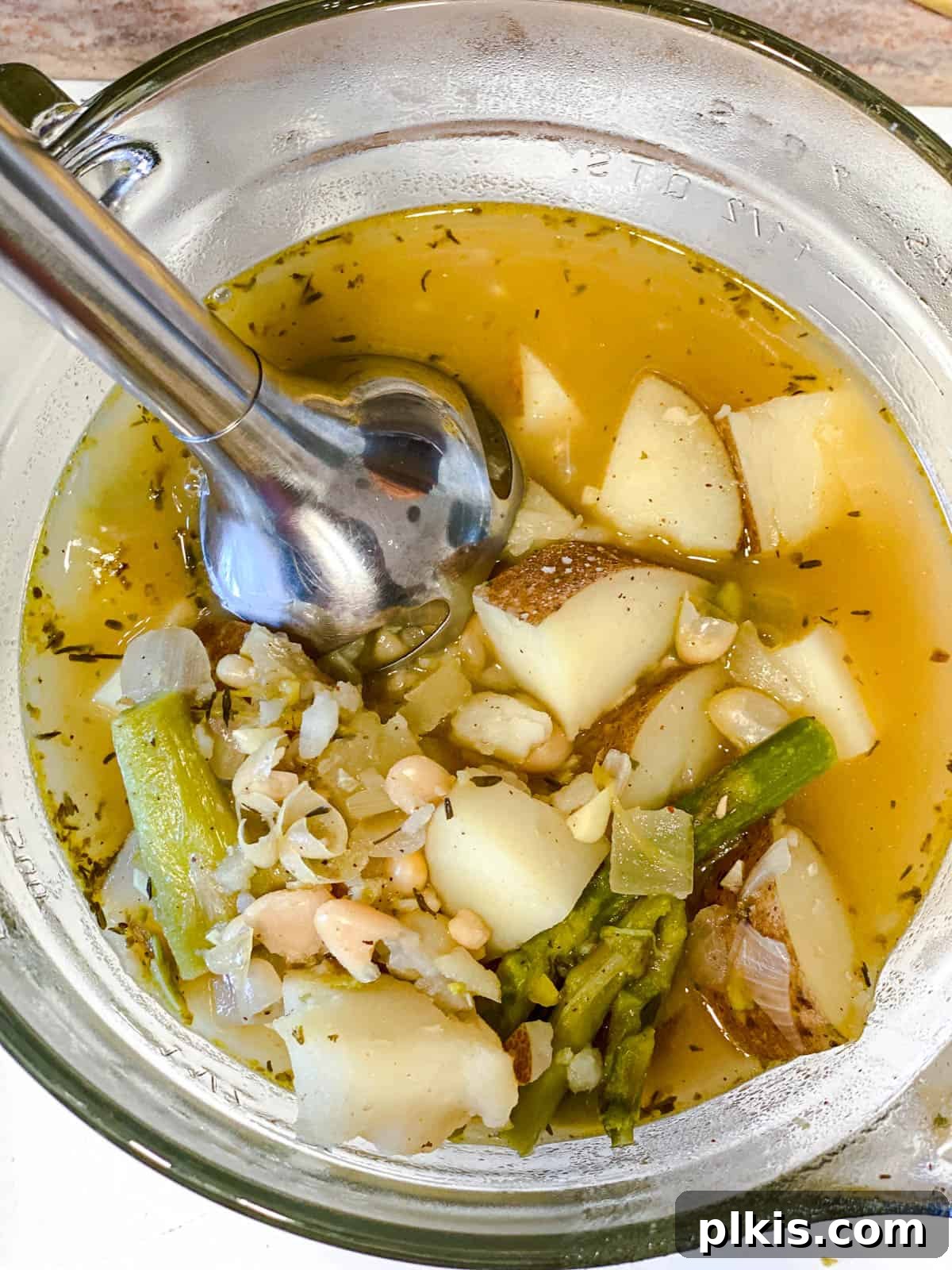 Process shot of using an immersion blender directly in the pot to puree half of the simmering asparagus soup, creating a creamy texture.