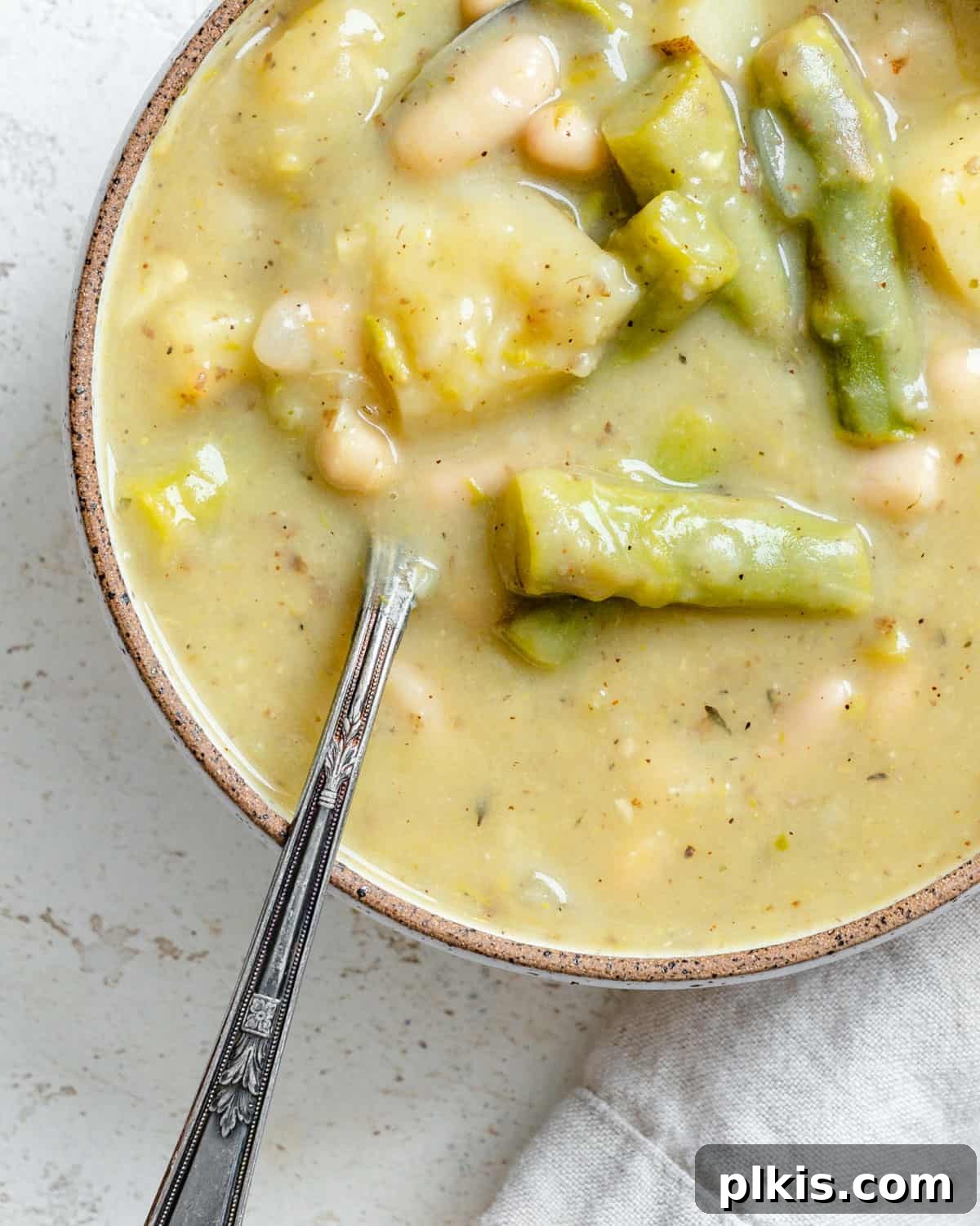 A close-up shot of a steaming bowl of creamy vegan asparagus soup, perfectly garnished with fresh dill and a sprinkle of black pepper, ready to be served.