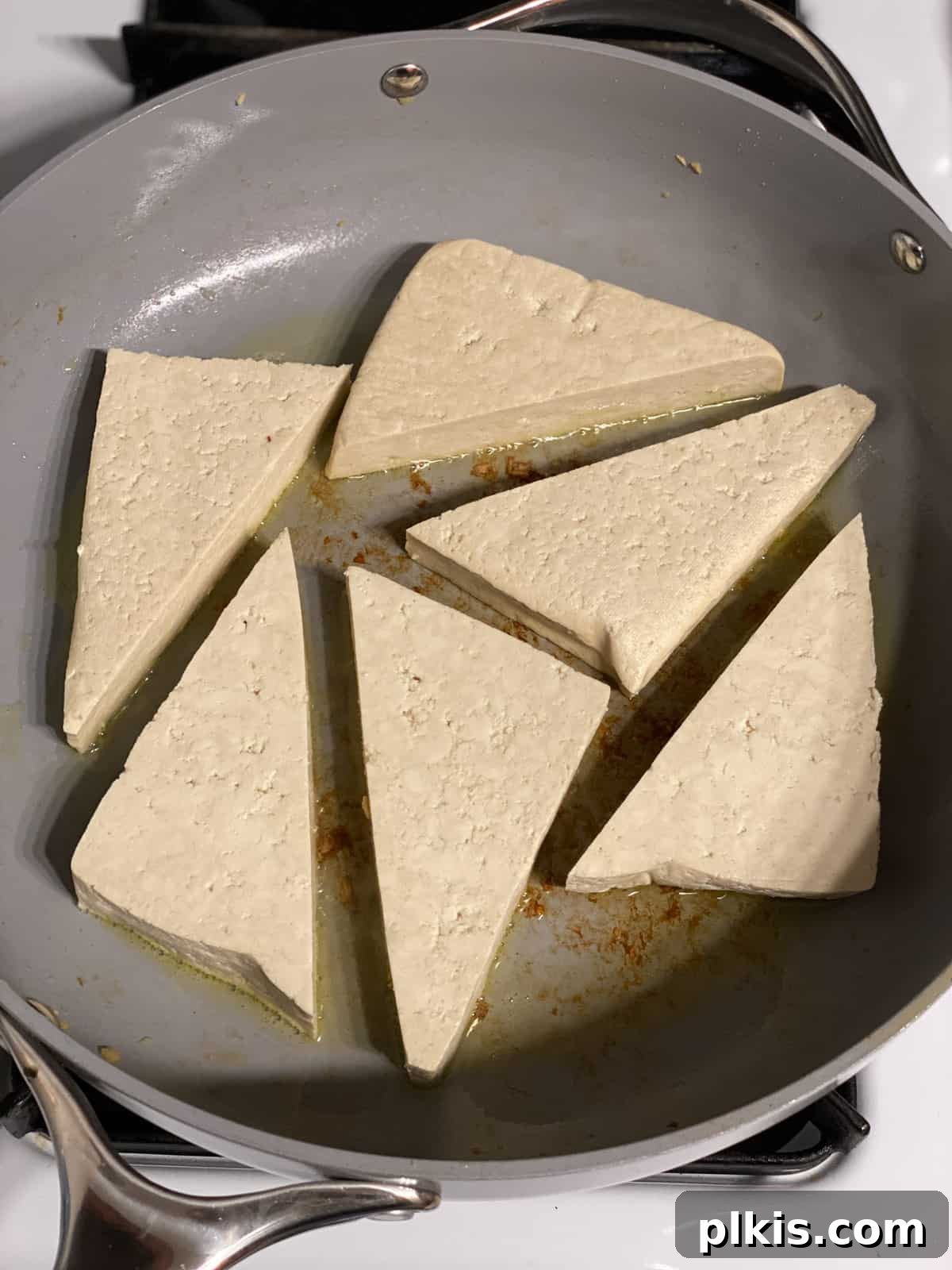 Vibrant Lemon Basil Tofu 7 Triangular tofu pieces being added to a frying pan, with sautéed vegetables pushed to the side.