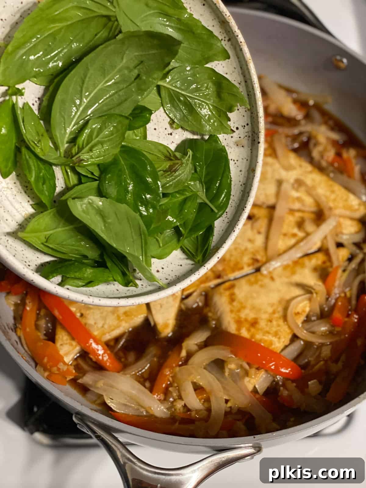 Vibrant Lemon Basil Tofu 8 Fresh basil leaves being added to the frying pan with tofu and vegetables, ready for the sauce.
