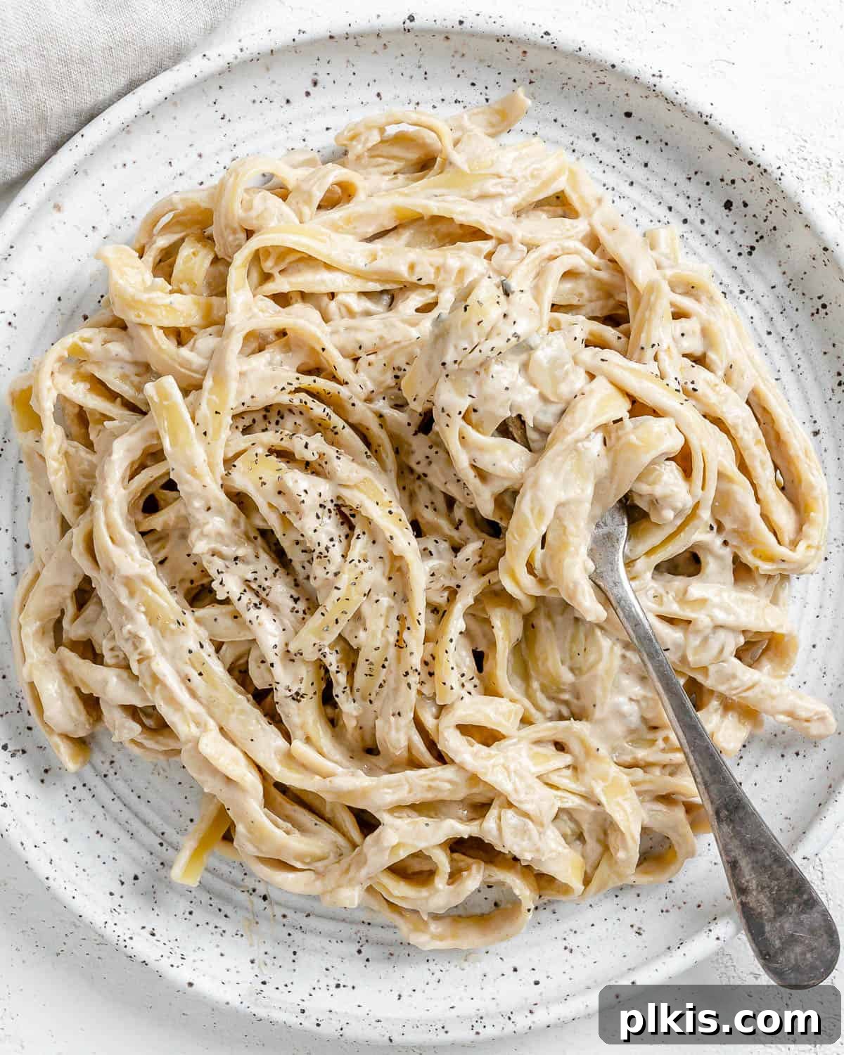 Decadent Vegan Fettuccine Alfredo 2 A beautifully plated dish of Vegan Fettuccine Alfredo, garnished with fresh parsley and cracked black pepper, set against a clean white background.