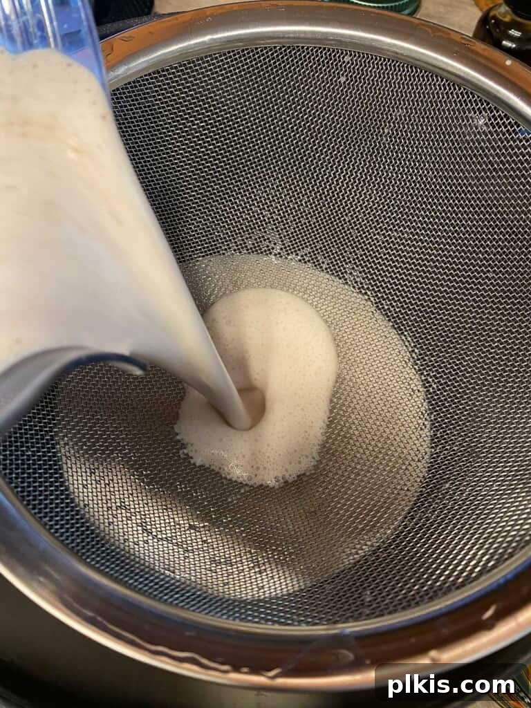 Decadent Vegan Fettuccine Alfredo 4 Process photo illustrating homemade almond milk being strained through a nut milk bag over a large bowl to separate pulp.