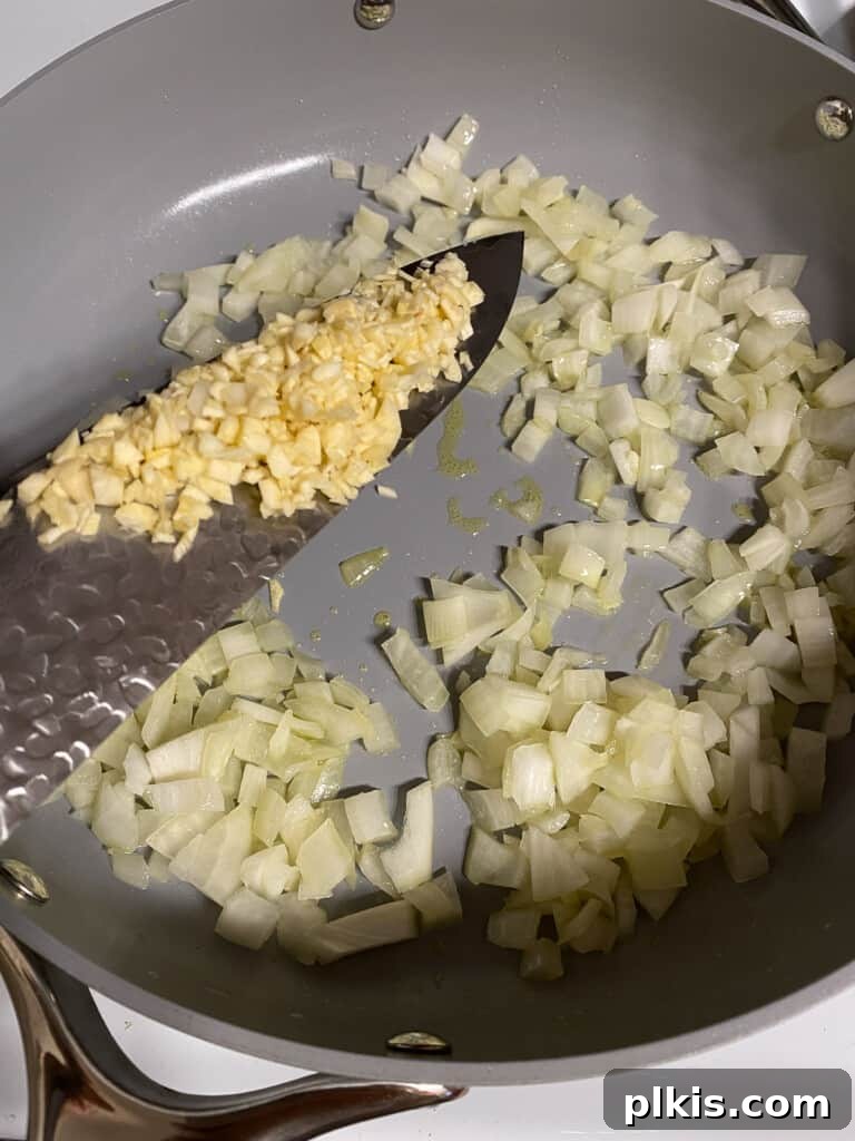 Decadent Vegan Fettuccine Alfredo 5 Process photo showing minced garlic being added to a pan with sautéed onions and oil, releasing its fragrant aroma.
