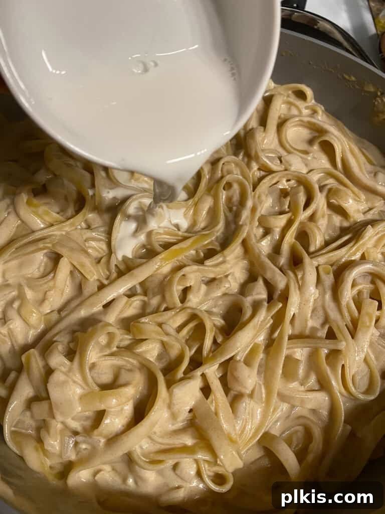 Decadent Vegan Fettuccine Alfredo 8 Process photo showing a cornstarch slurry being stirred into a pot of cooking pasta and Alfredo sauce to thicken it.