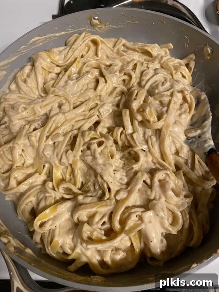 Decadent Vegan Fettuccine Alfredo 9 Process photo showing a wooden spoon stirring creamy fettuccine pasta in a large pot, ensuring the sauce is evenly distributed and thickening.