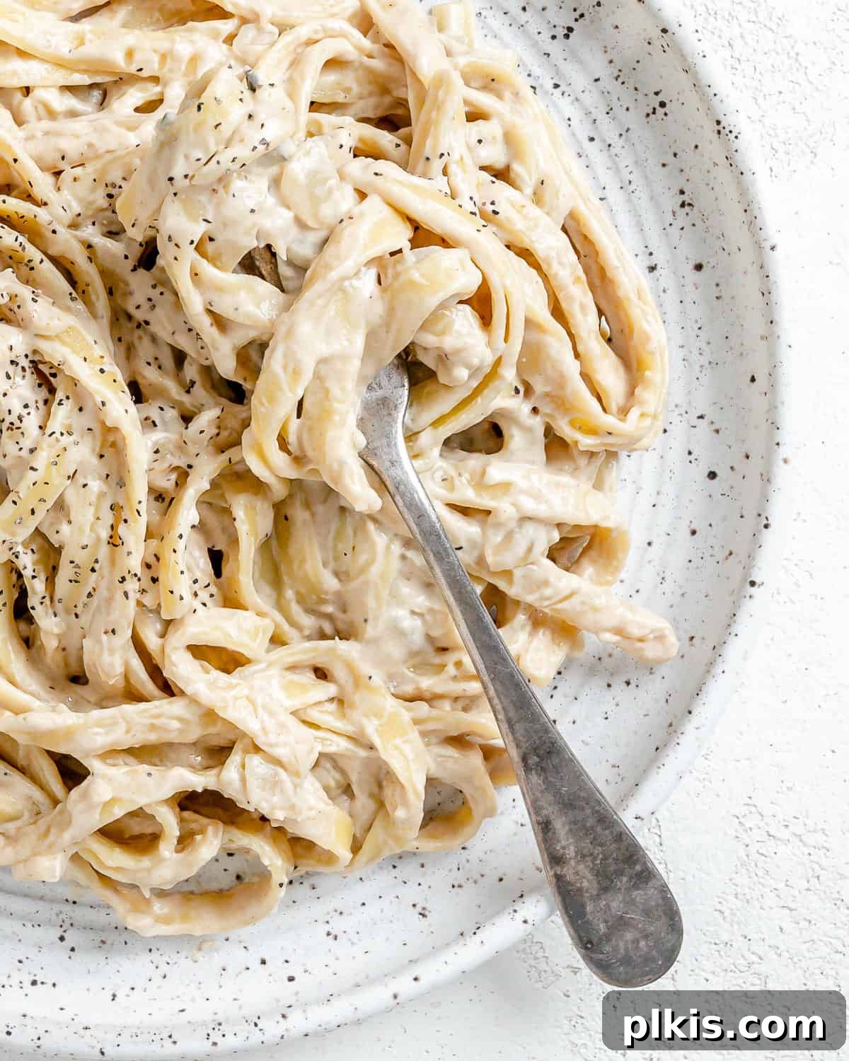 Decadent Vegan Fettuccine Alfredo 10 A close-up shot of the finished Vegan Fettuccine Alfredo, showcasing its creamy texture and fresh garnishes on a white plate, ready to be enjoyed.