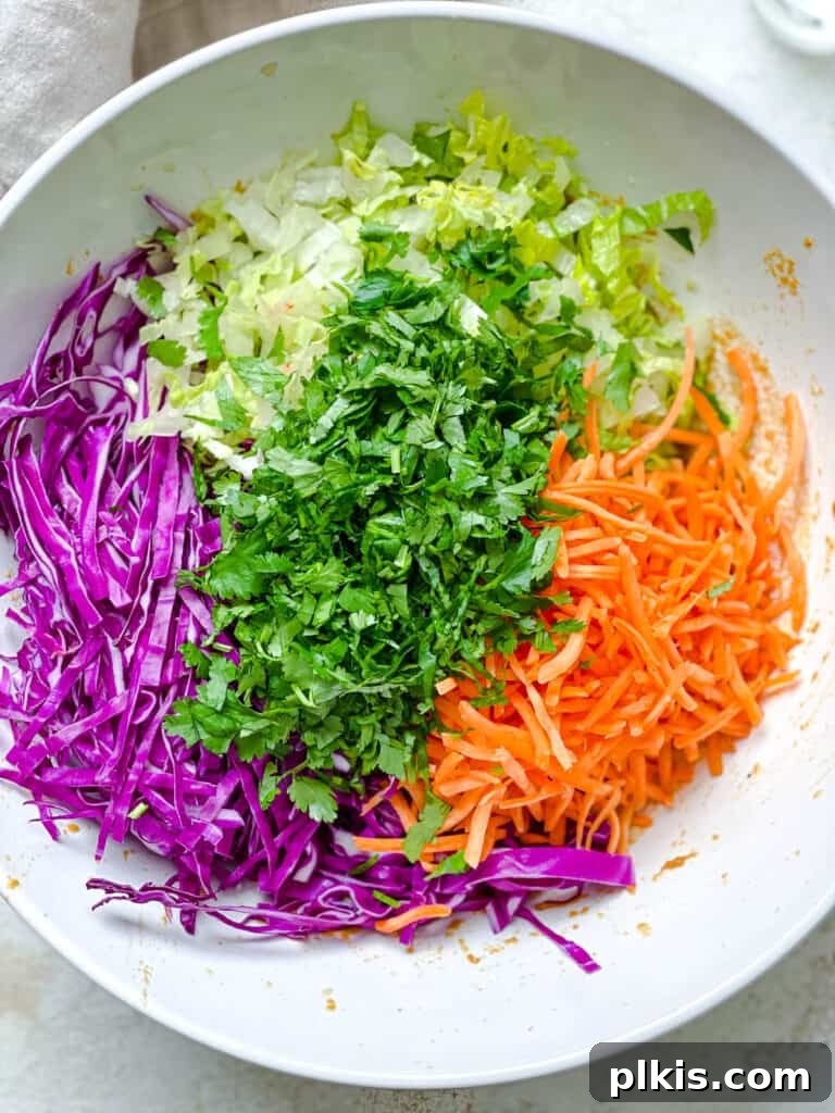Zesty Thai Peanut Salad 5 A process shot demonstrating various fresh, shredded vegetables being combined in a large mixing bowl.