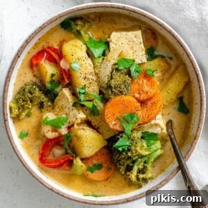Bowl with Tofu Yellow Curry over a white textured surface with a spoon in it.