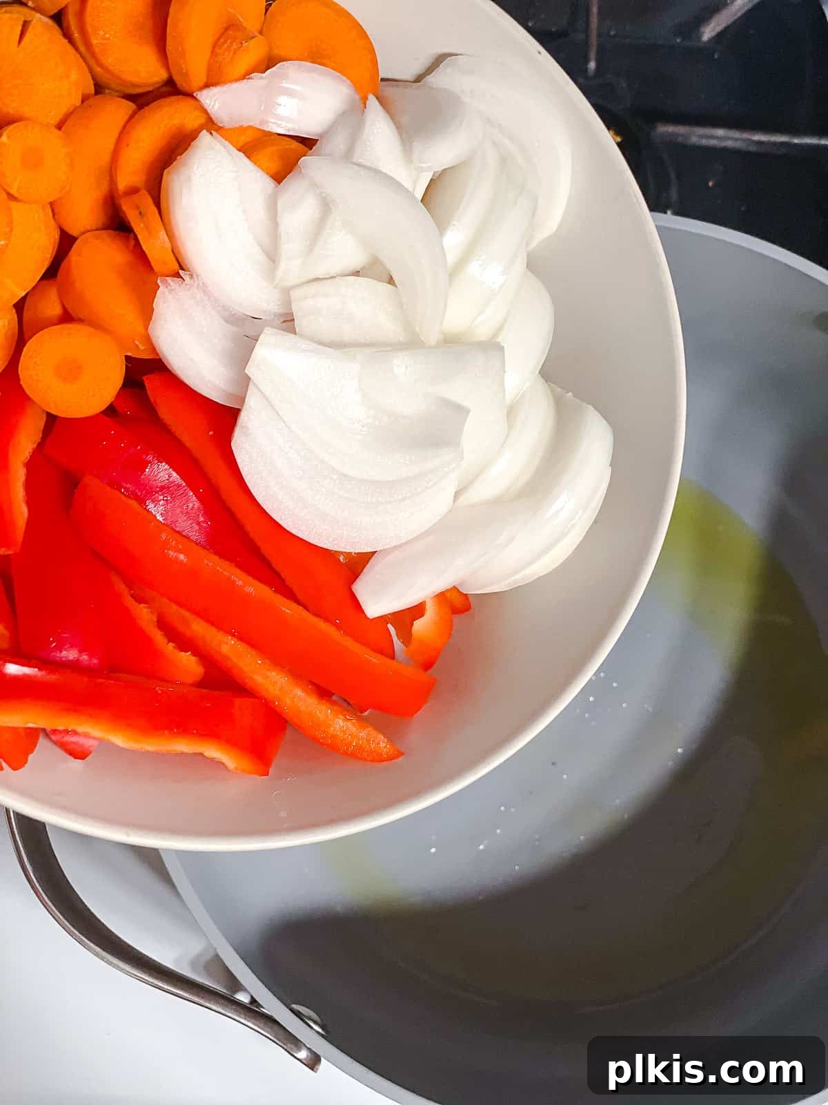 Creamy One-Pot Vegan Yellow Tofu Curry 5 Sliced onions, carrots, and red bell peppers being added to a large pot with heated oil, beginning the sautéing process.