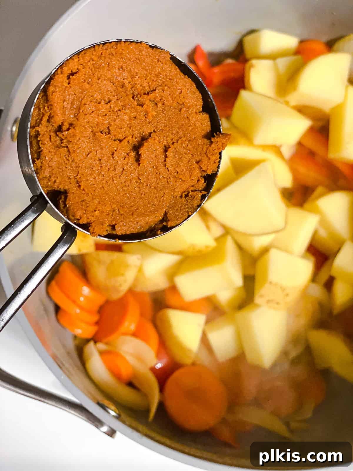 Creamy One-Pot Vegan Yellow Tofu Curry 6 Yellow curry paste being stirred into a pot with sautéed mixed vegetables and a small amount of oil, creating a fragrant mixture.