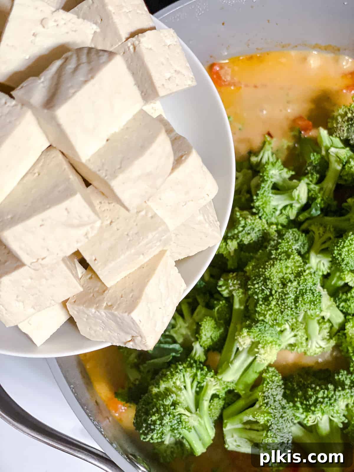 Creamy One-Pot Vegan Yellow Tofu Curry 7 Cubed tofu being gently added to a pot of simmering, creamy coconut yellow curry with mixed vegetables.