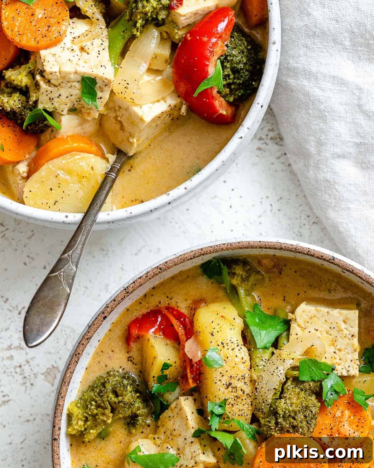 Creamy One-Pot Vegan Yellow Tofu Curry 8 A close-up view of a bowl of Tofu Yellow Curry, showcasing its rich, creamy sauce and colorful vegetables, with a spoon nestled in the bowl.