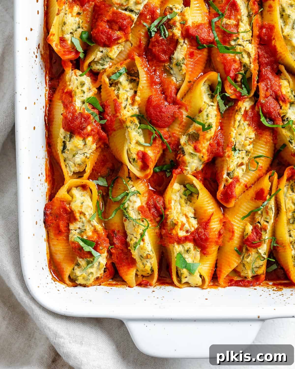 Creamy Vegan Stuffed Shells 2 Golden-brown Vegan Stuffed Shells baked in a white casserole dish, ready to be served, against a clean white background.