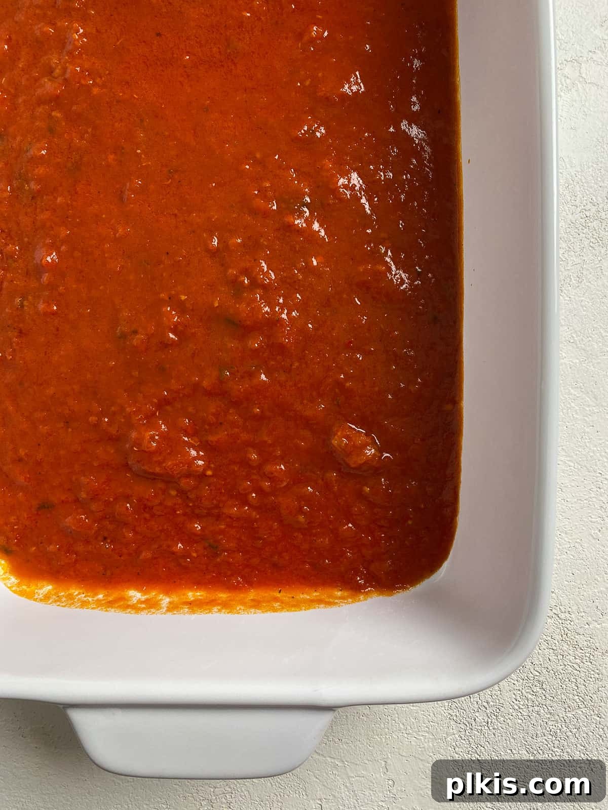 Creamy Vegan Stuffed Shells 11 Marinara sauce evenly spread across the bottom of a white baking dish, forming the flavorful bed for the stuffed shells.