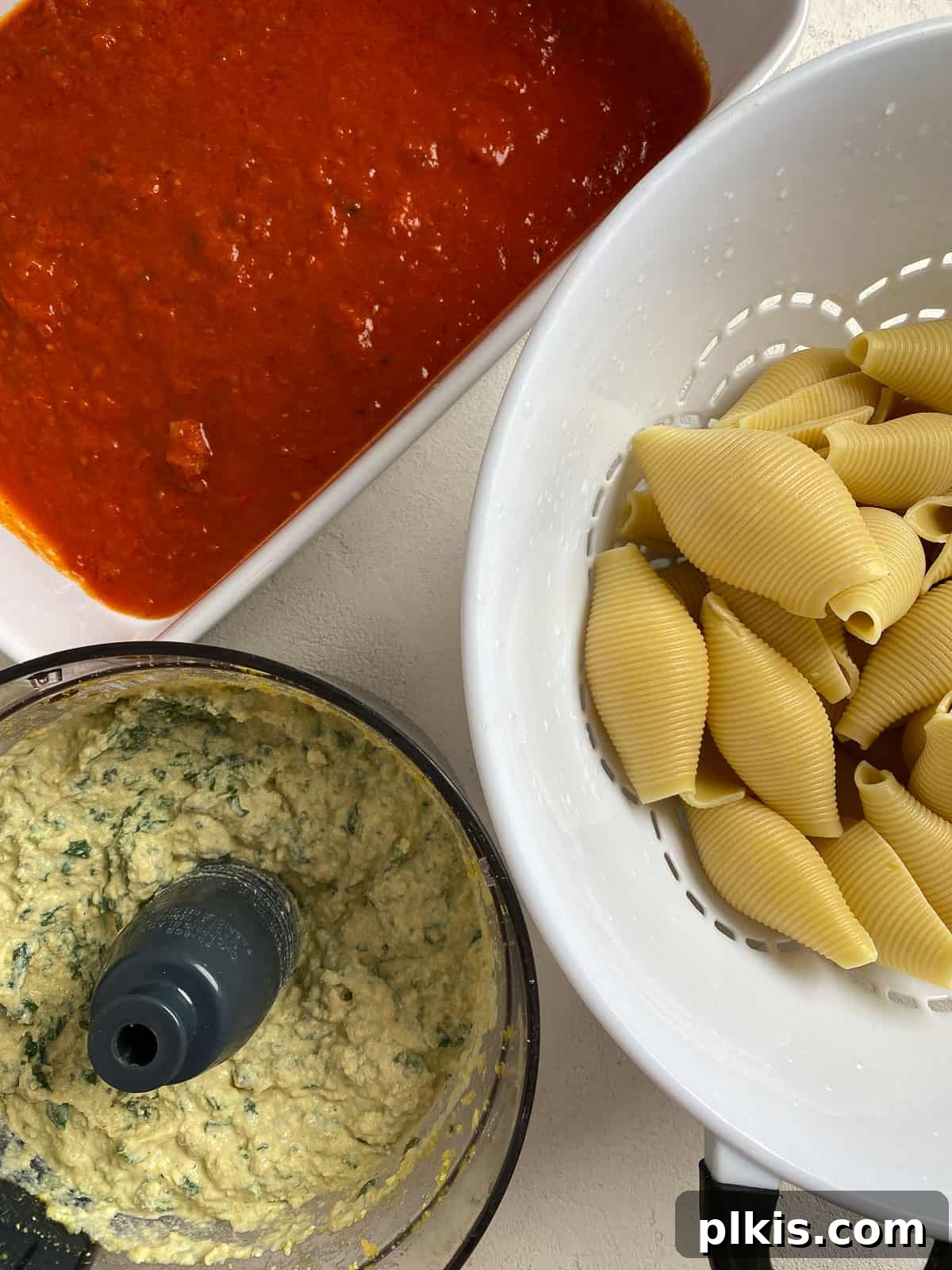 Creamy Vegan Stuffed Shells 12 An overview of the kitchen setup, with marinara in the baking dish, cooked shells in a colander, and the tofu ricotta filling ready in the food processor.