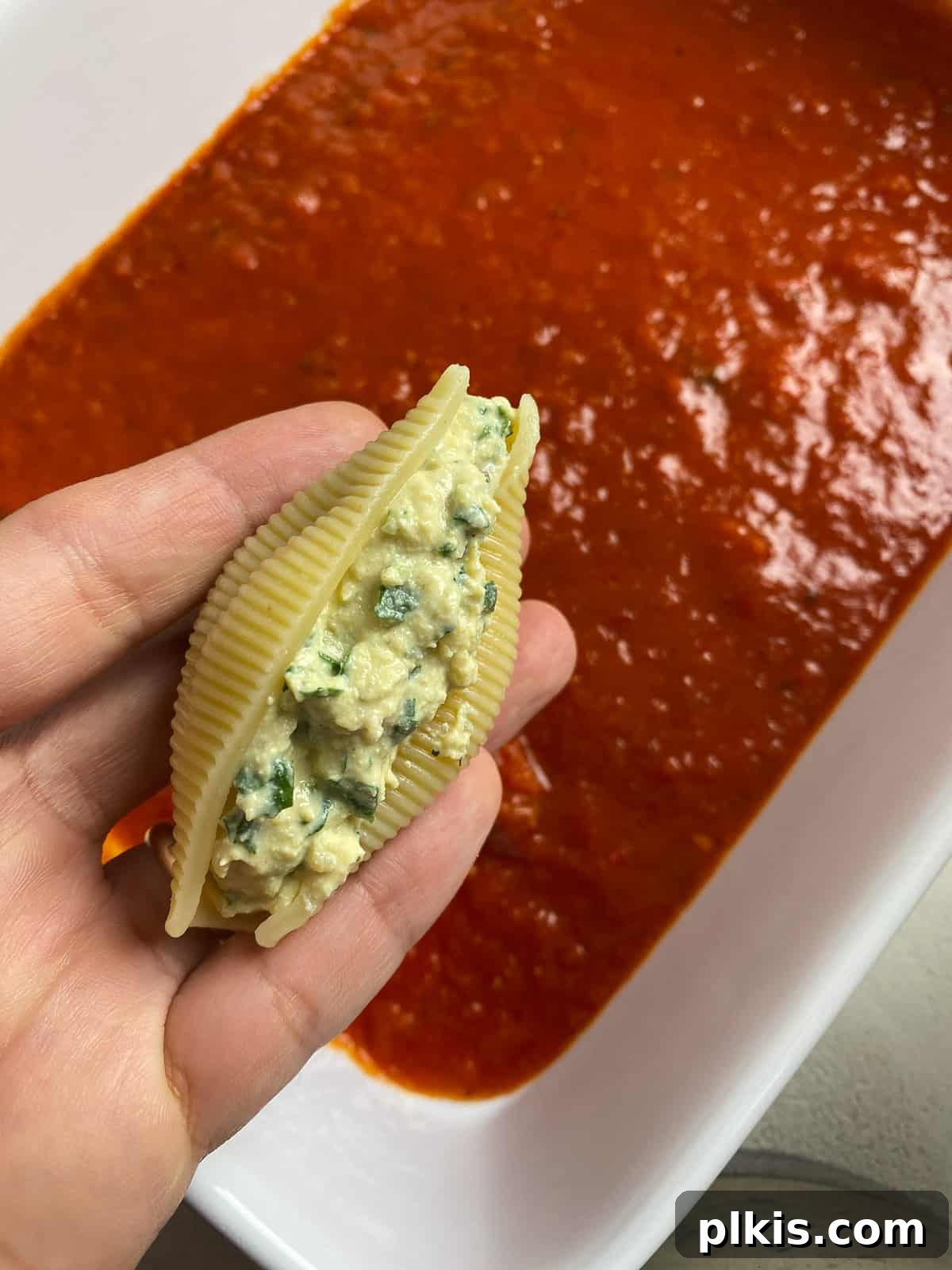Creamy Vegan Stuffed Shells 13 A stuffed pasta shell being carefully placed into the marinara-lined baking dish.