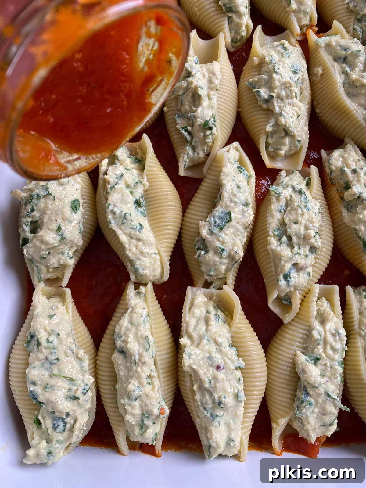 Creamy Vegan Stuffed Shells 15 The remaining marinara sauce being drizzled over the assembled stuffed shells in the baking dish.