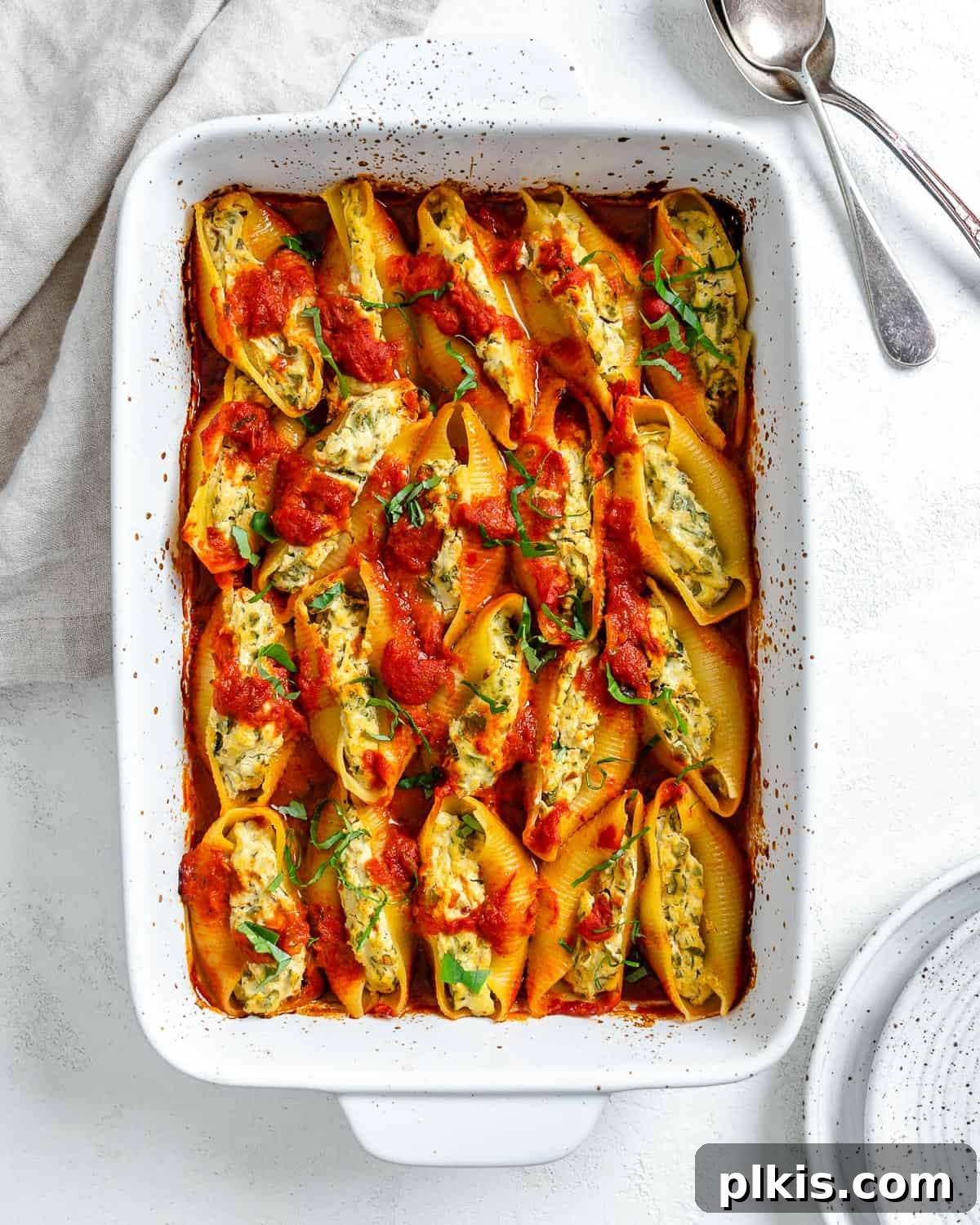 Creamy Vegan Stuffed Shells 18 Close-up of a serving of baked Vegan Stuffed Shells in a white dish, garnished with fresh basil, against a soft background.