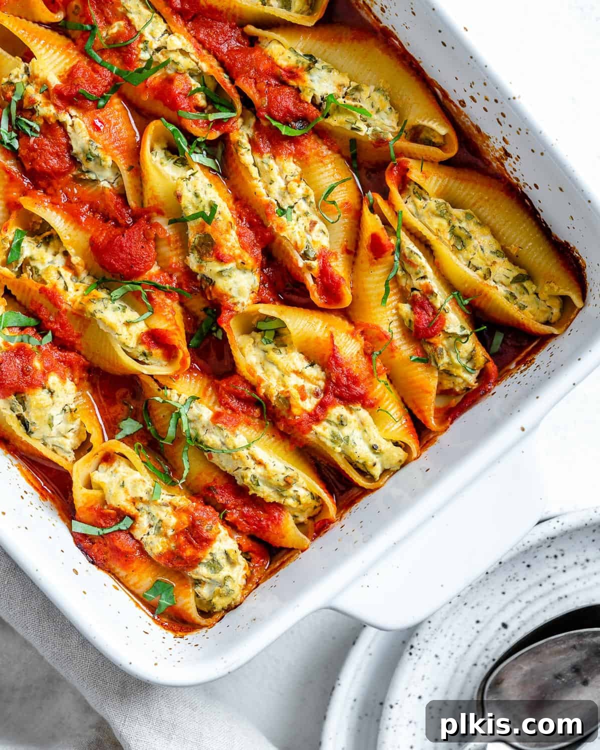 Creamy Vegan Stuffed Shells 19 A large white baking dish filled with beautifully baked Vegan Stuffed Shells, garnished with fresh basil, presented on a white background.
