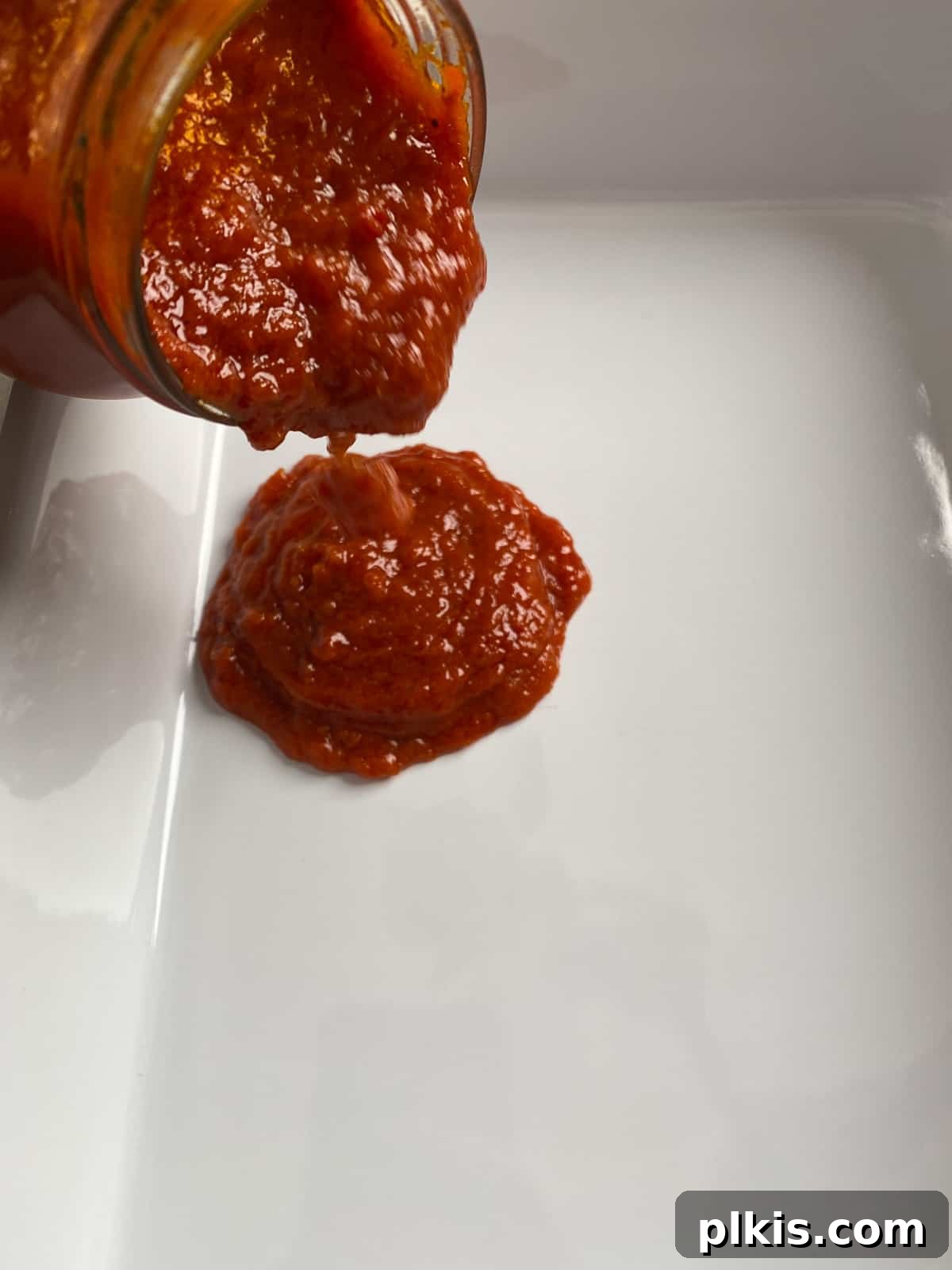 Creamy Vegan Stuffed Shells 10 Marinara sauce being poured into a white ceramic baking dish, ready to be spread as the base for the stuffed shells.