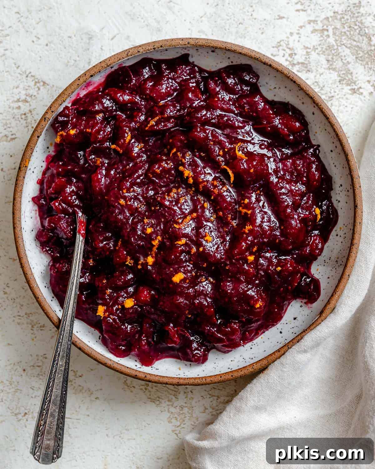 A vibrant bowl of Easy Cranberry Sauce with Orange Juice, garnished with fresh cranberries and orange slices, sitting on a white surface, ready to be served.