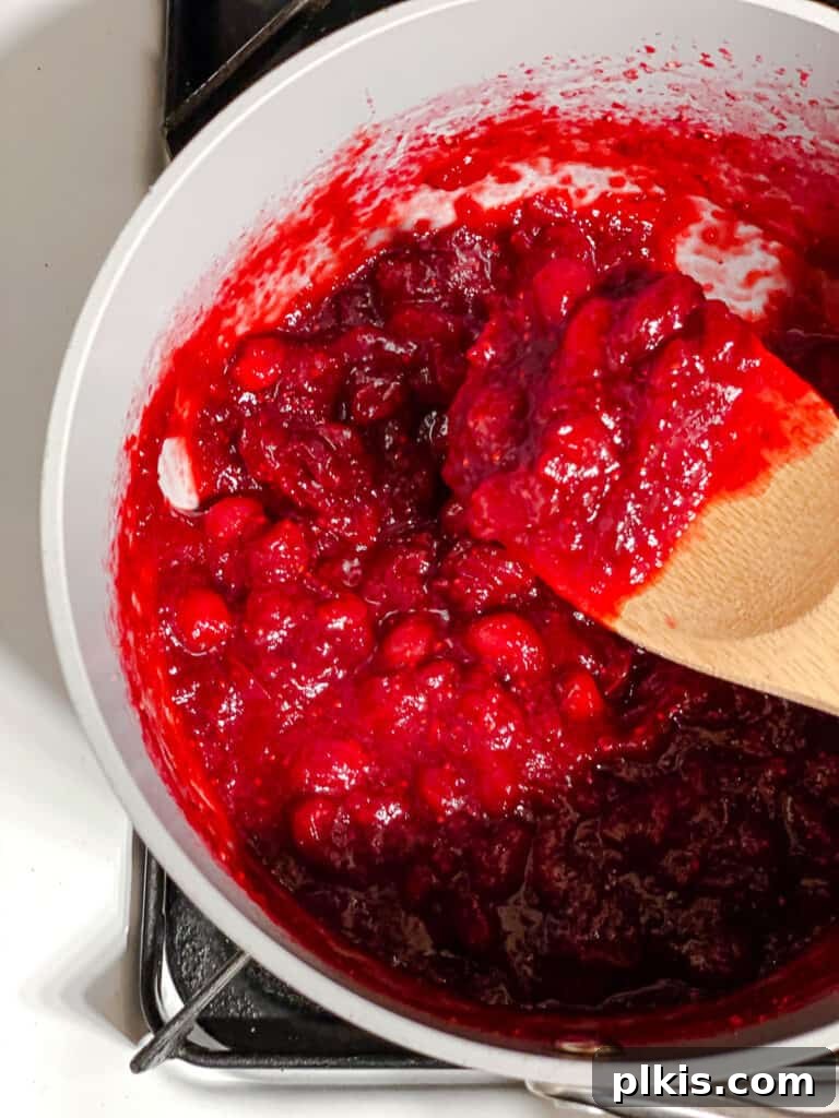 Process shot of cranberries cooking in a pot, simmering in the orange-sugar liquid, illustrating the key cooking phase.