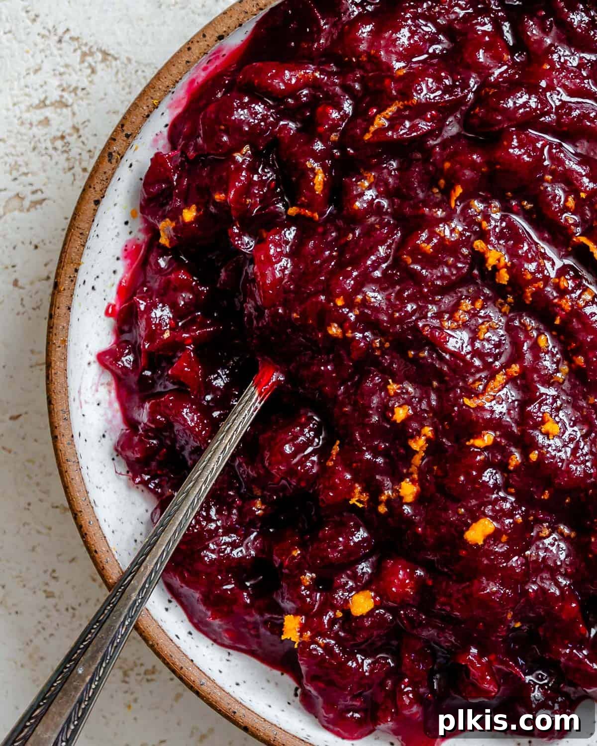 A bowl of vibrant, complete Easy Cranberry Sauce with Orange Juice, garnished with fresh cranberries and a sprig of rosemary, on a pristine white surface, ready for serving.