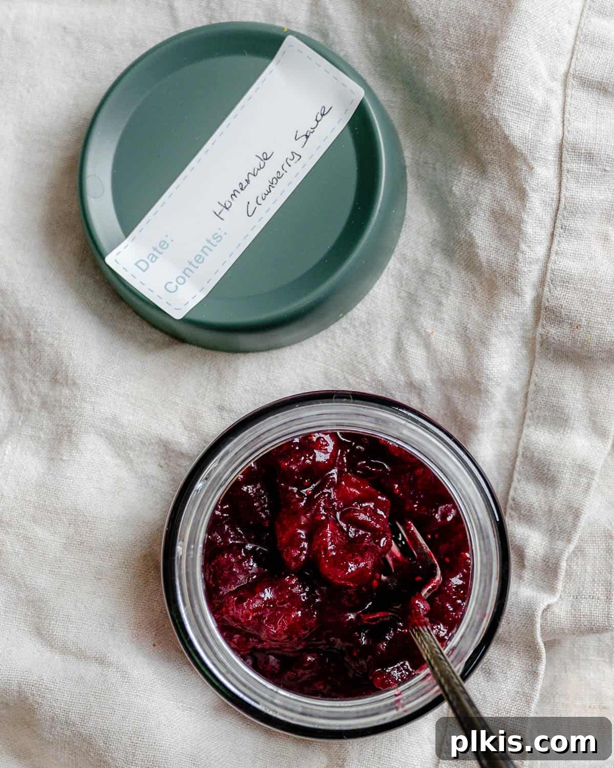 Easy Cranberry Sauce with Orange Juice in a clear storage container, garnished with a sprig of rosemary, on a white surface, highlighting its freshness and vibrant color.