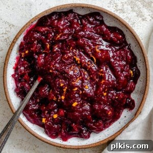 Complete Easy Cranberry Sauce with Orange Juice in a small bowl, garnished with fresh orange slices and cranberries.