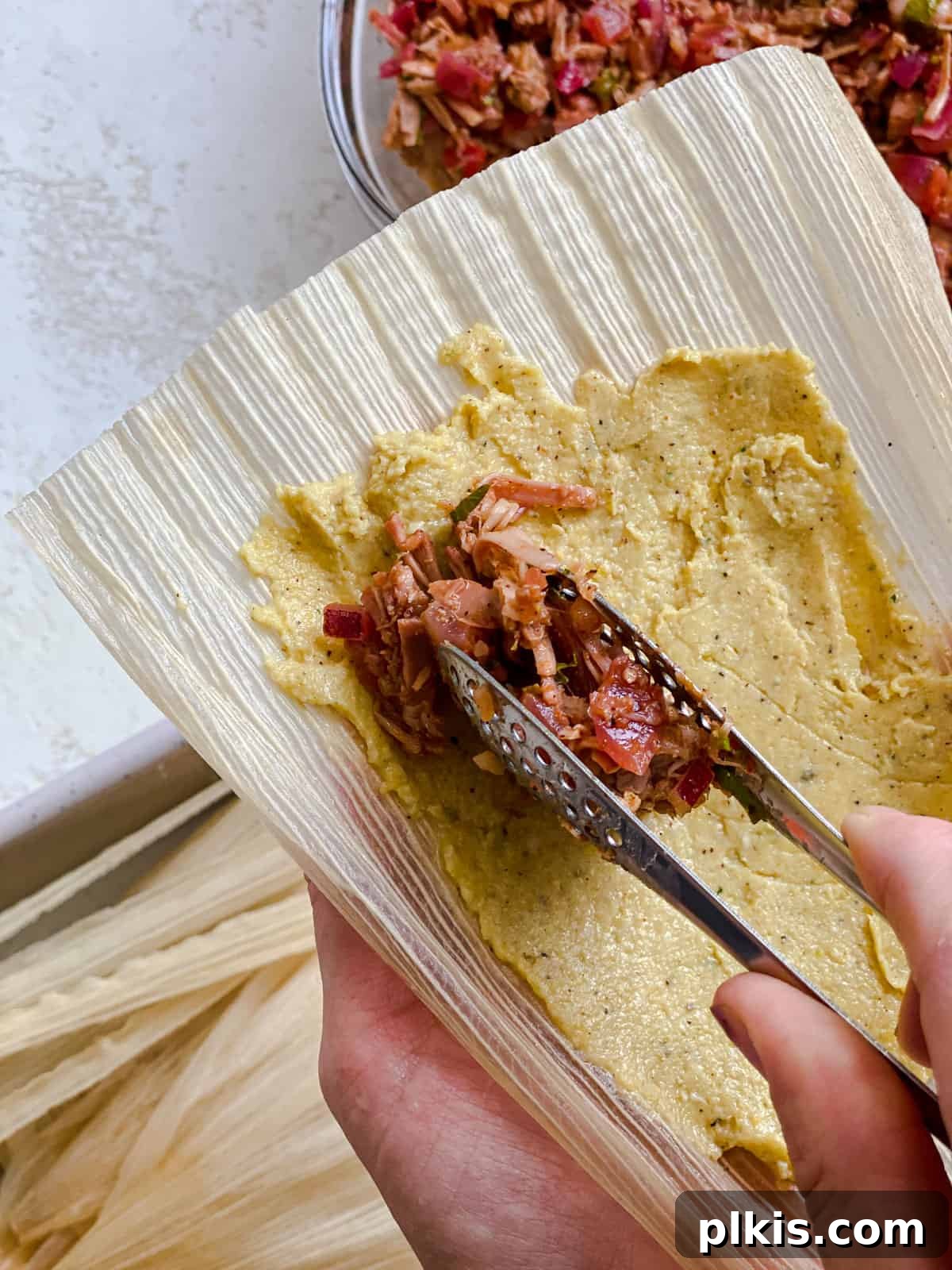 Crafting Perfect Vegan Tamales 12 Process shot of adding the filling mixture vertically into the center of the masa on a corn husk.