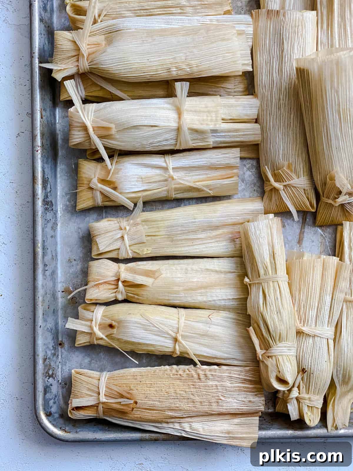 Crafting Perfect Vegan Tamales 14 Several pre-cooked tamales, neatly folded and tied, arranged in a baking dish.