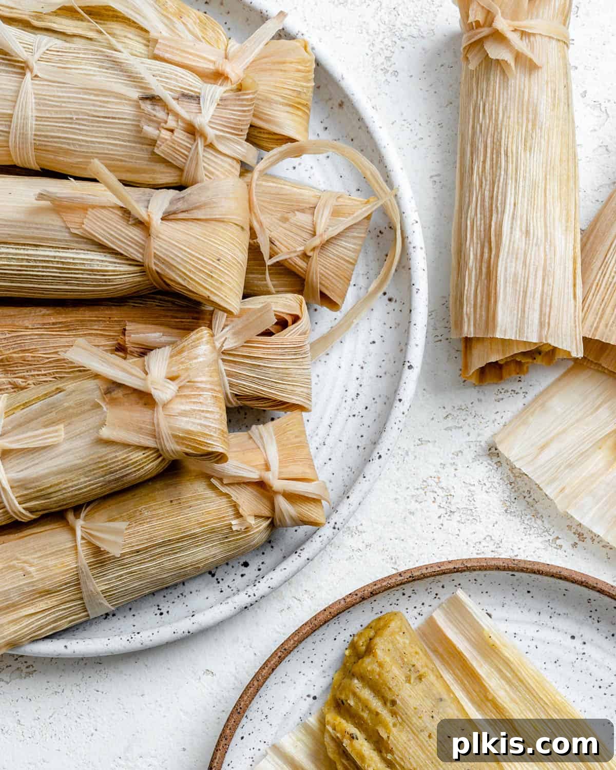 Crafting Perfect Vegan Tamales 16 Several completed vegan tamales artfully arranged on a plate, set against a white backdrop.