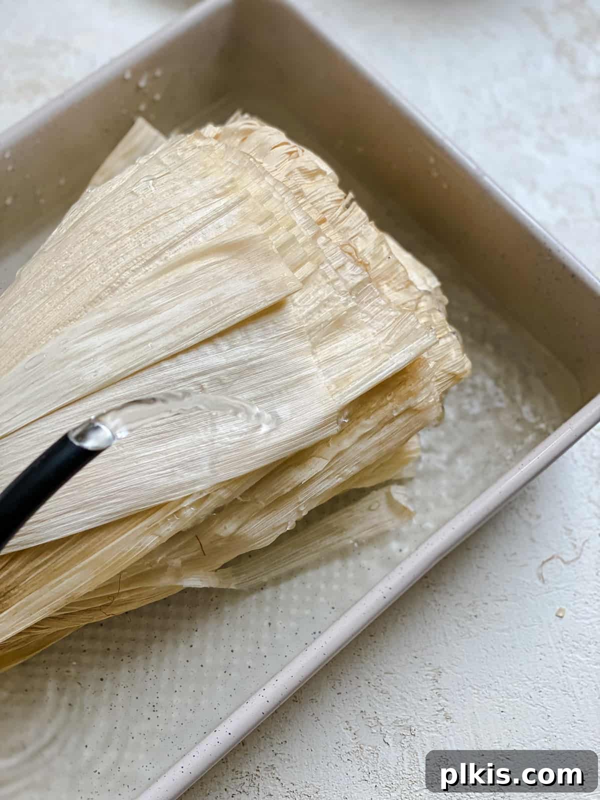 Crafting Perfect Vegan Tamales 4 Process shot showing dried corn husks soaking in hot water in a baking dish.