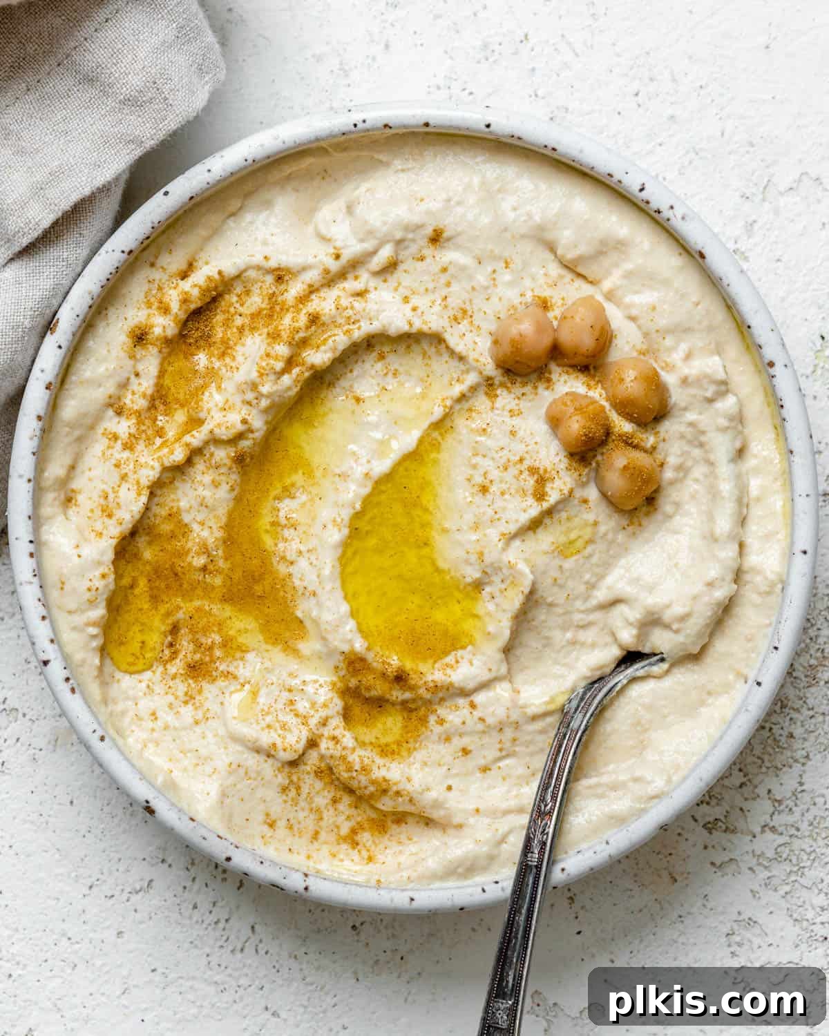 Quick & Creamy Hummus 2 A bowl of freshly made, creamy easy hummus, garnished with a drizzle of olive oil and a sprinkle of paprika, set against a light, inviting background.
