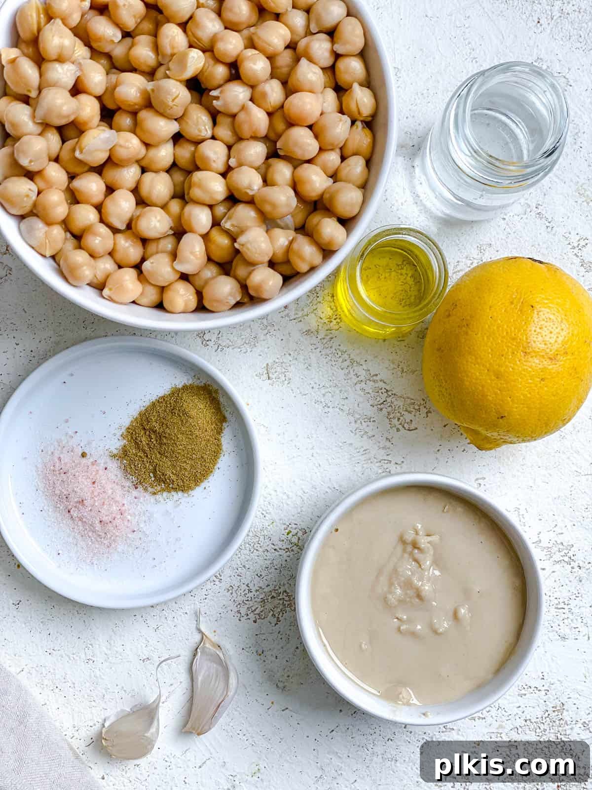 Quick & Creamy Hummus 3 All six essential ingredients for easy homemade hummus, including canned chickpeas, tahini, lemon, garlic, cumin, and salt, neatly arranged against a clean white background.