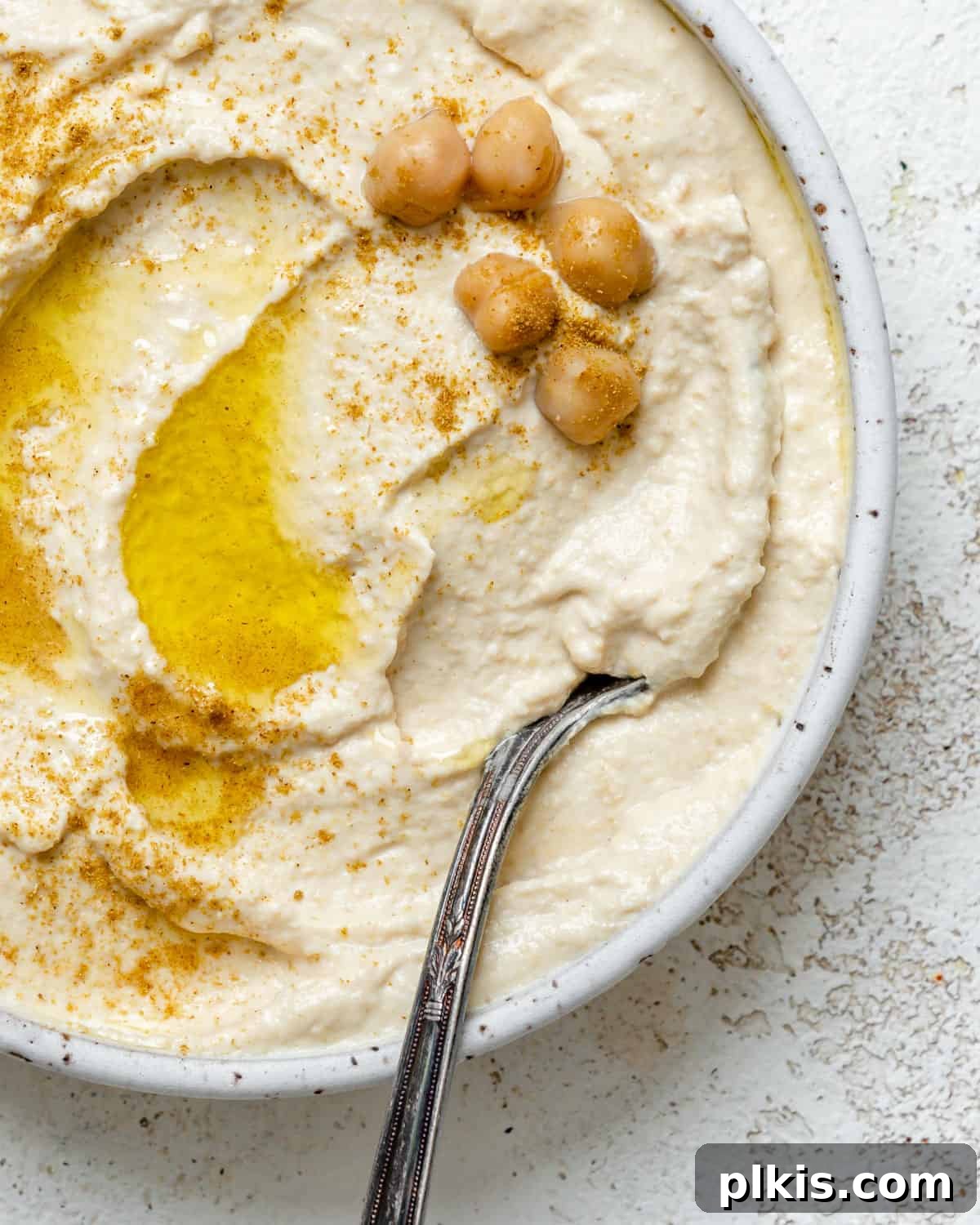 Quick & Creamy Hummus 7 A beautifully presented bowl of creamy homemade hummus, garnished with olive oil and spices, on a rustic wooden board, ready to be served.