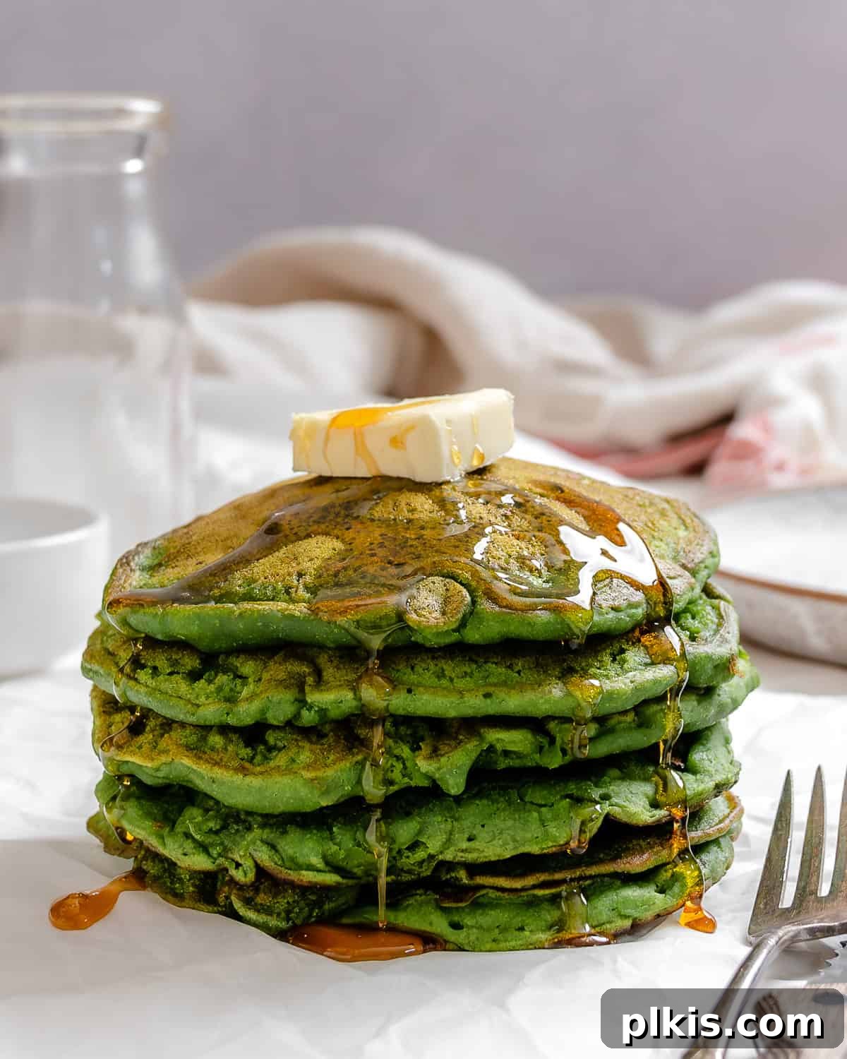 Green Power Banana Pancakes 2 A beautifully stacked plate of vibrant green Banana Spinach Pancakes, garnished with fresh berries and a drizzle of maple syrup, against a light backdrop.