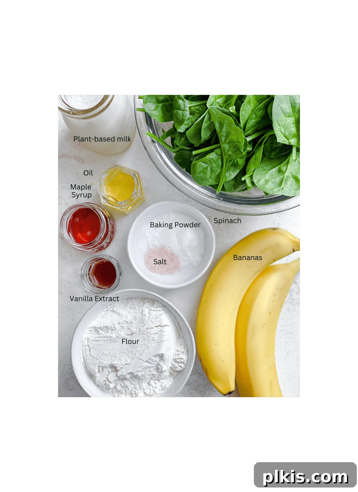 Green Power Banana Pancakes 3 A selection of fresh ingredients laid out on a white surface, including spinach, bananas, plant-based milk, and flour, ready for making Easy Banana Spinach Pancakes.
