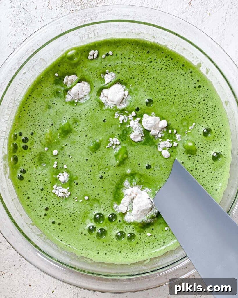 Green Power Banana Pancakes 5 A large mixing bowl containing mashed bananas, flour, and other dry ingredients, with the green spinach-infused milk being poured in, ready for whisking.