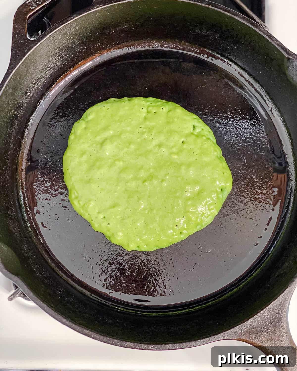 Green Power Banana Pancakes 7 A spatula flipping a green banana spinach pancake on a hot non-stick pan, showing the golden-brown underside.