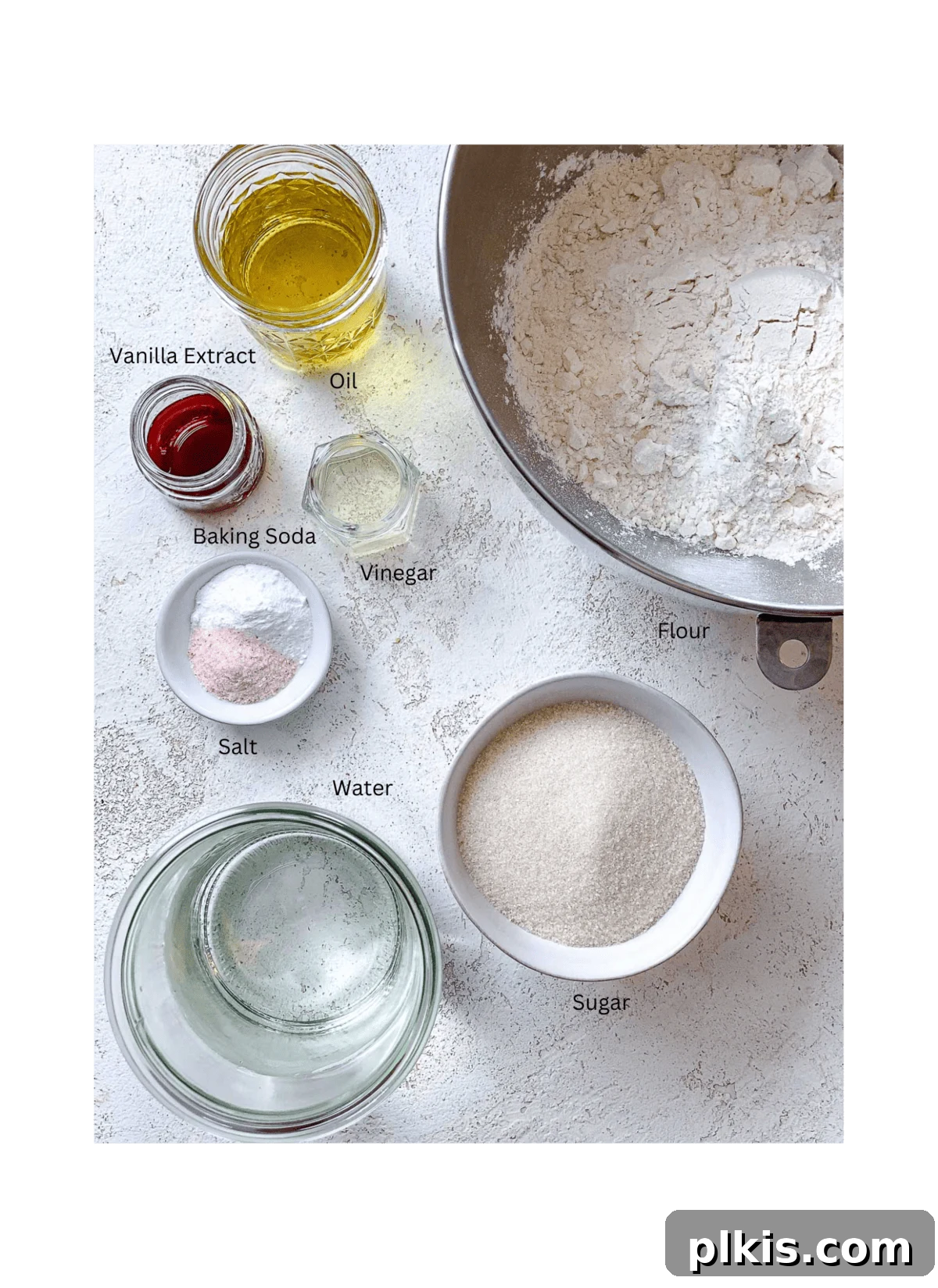 Effortless Vegan Vanilla Cupcakes 3 ingredients for Easy Vegan Vanilla Cupcakes measured out against a white surface, clearly showing flour, sugar, oil, vanilla, and other core components