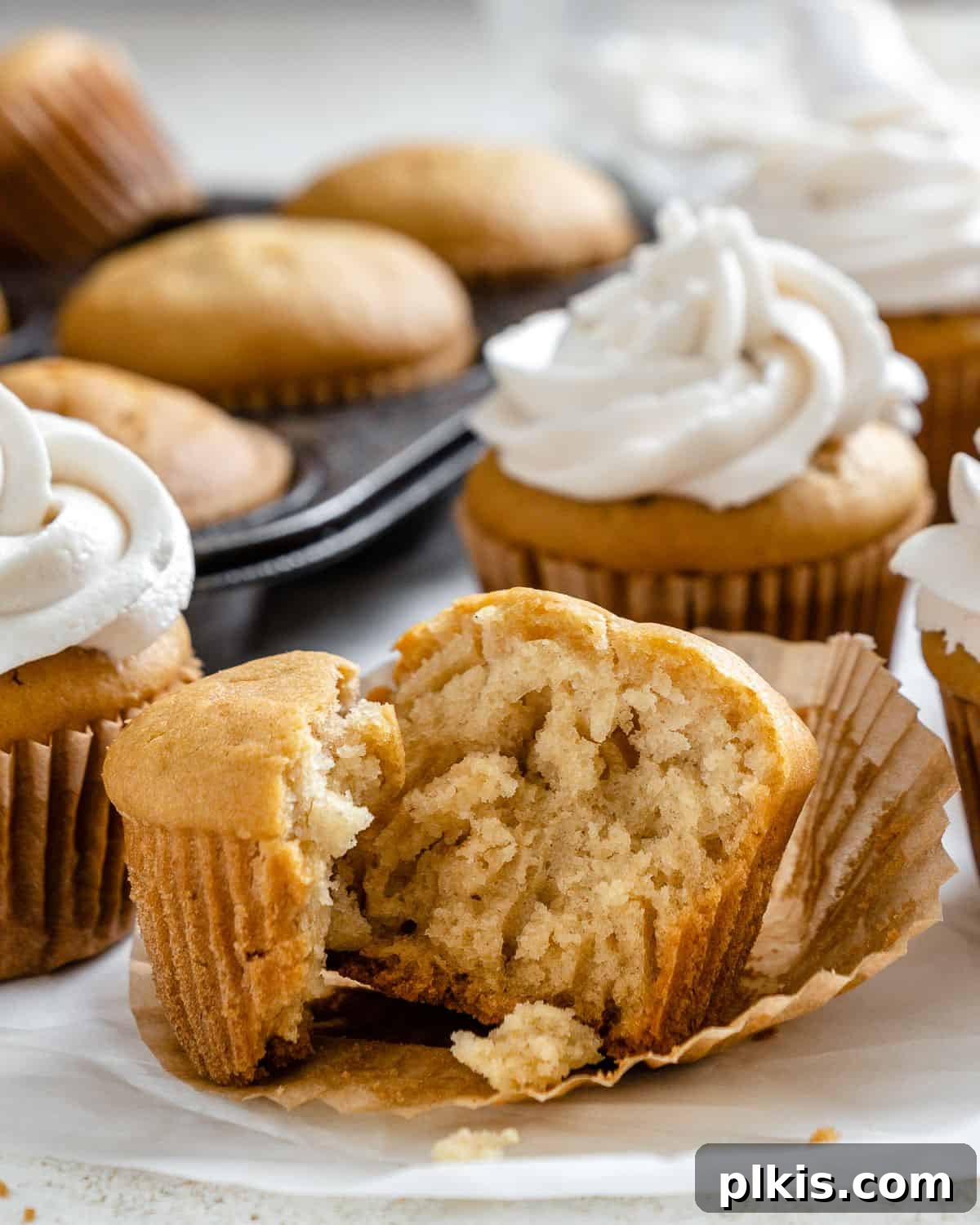Effortless Vegan Vanilla Cupcakes 8 close up of an opened vegan vanilla cupcake, revealing its moist and fluffy interior, with frosted cupcakes in the background