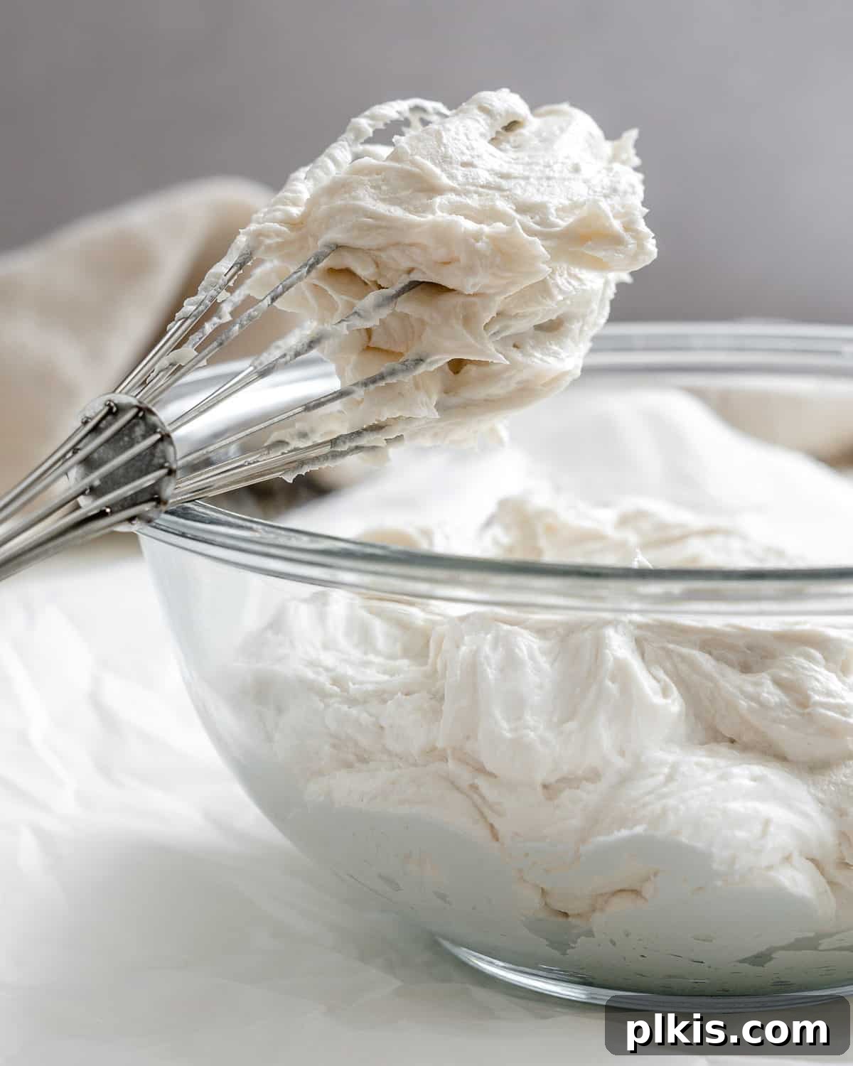 Velvety Vegan Vanilla Buttercream 2 A bowl of fluffy vanilla vegan buttercream frosting with a whisk resting in it, showcasing its creamy texture.