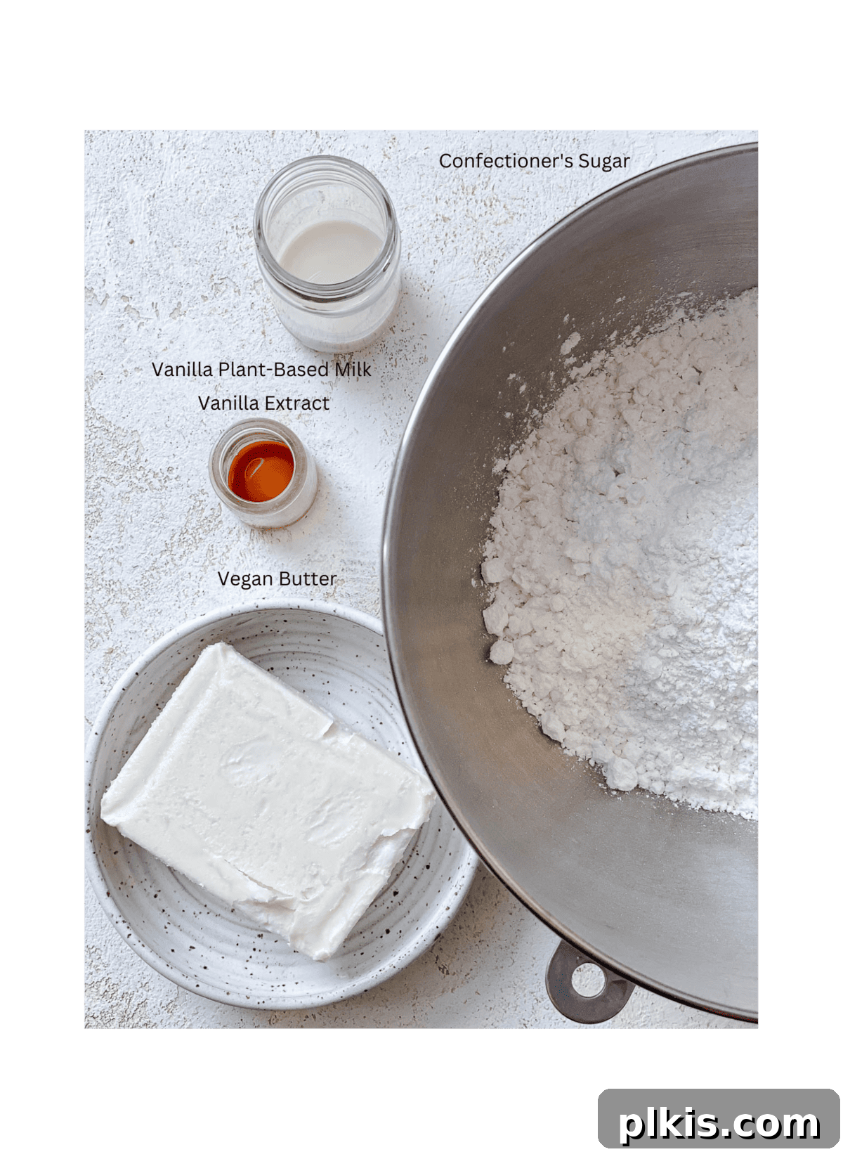 Velvety Vegan Vanilla Buttercream 3 A collection of ingredients for Vanilla Vegan Buttercream Frosting laid out on a white surface, including powdered sugar, vegan butter, vanilla extract, and plant-based milk.