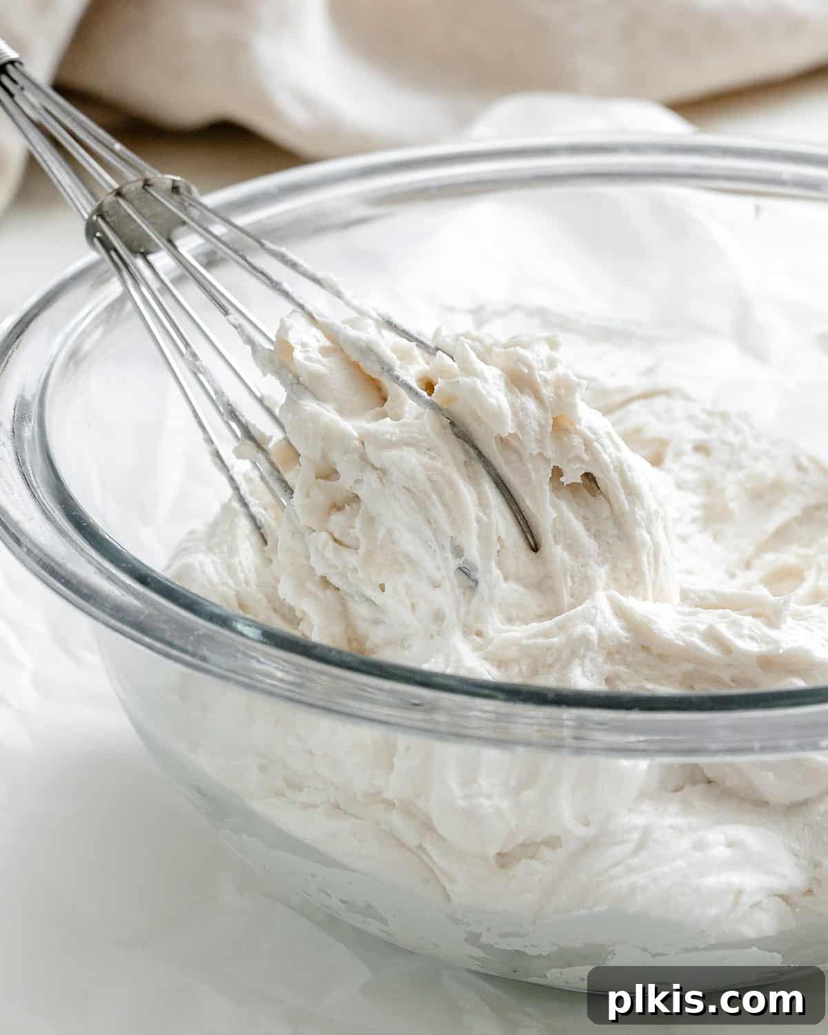 Velvety Vegan Vanilla Buttercream 6 Completed Vanilla Vegan Buttercream Frosting in a glass bowl, showcasing its smooth and inviting texture, with a whisk nearby.
