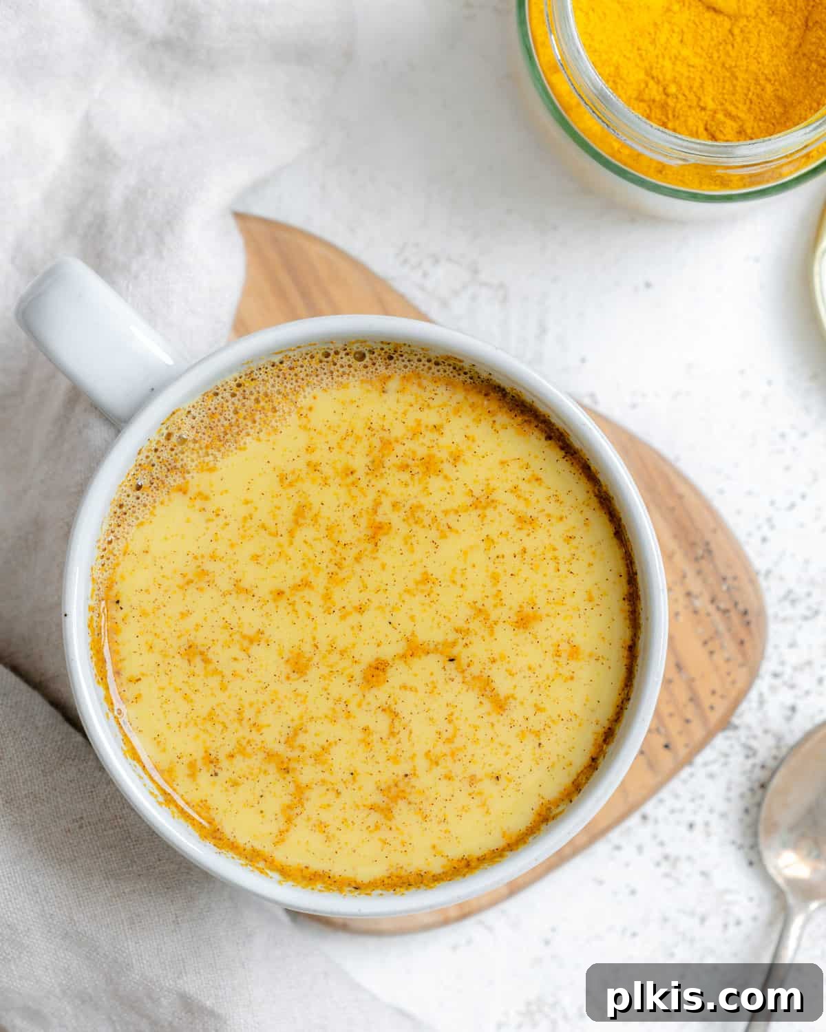 A warm cup of Turmeric Golden Milk [Haldi Doodh] set against a soft white background, inviting and comforting.