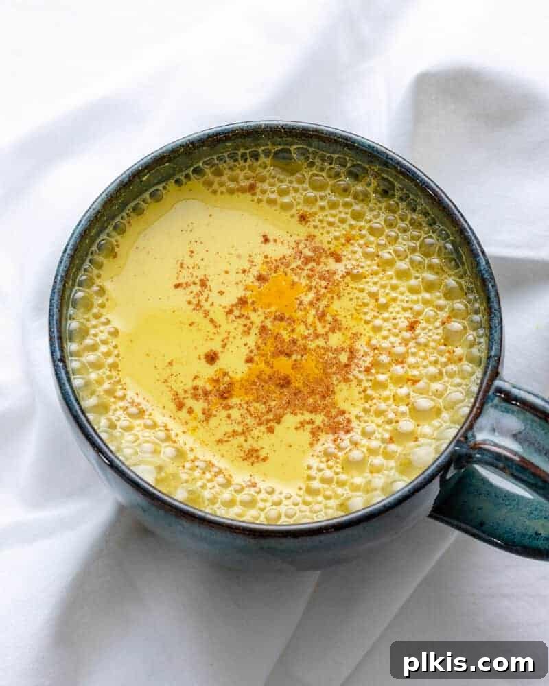 Golden Turmeric Elixir 9 A comforting cup of golden milk in a dark-colored mug, set against a pristine white background, highlighting its rich color.