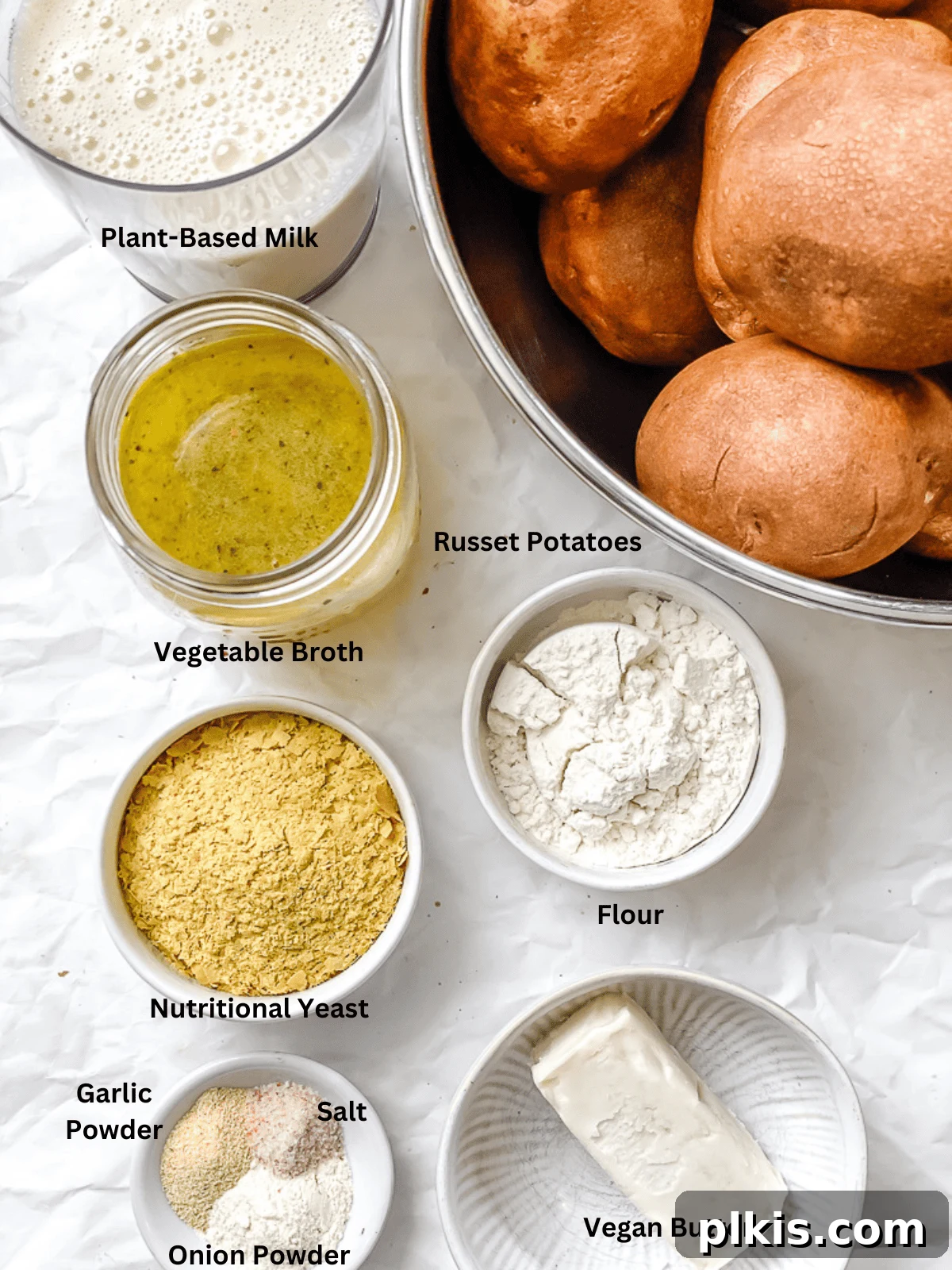 Decadent Dairy-Free Scalloped Potatoes 3 Individual bowls containing the ingredients for vegan scalloped potatoes, including sliced potatoes, vegan butter, flour, plant milk, vegetable broth, nutritional yeast, and seasonings.