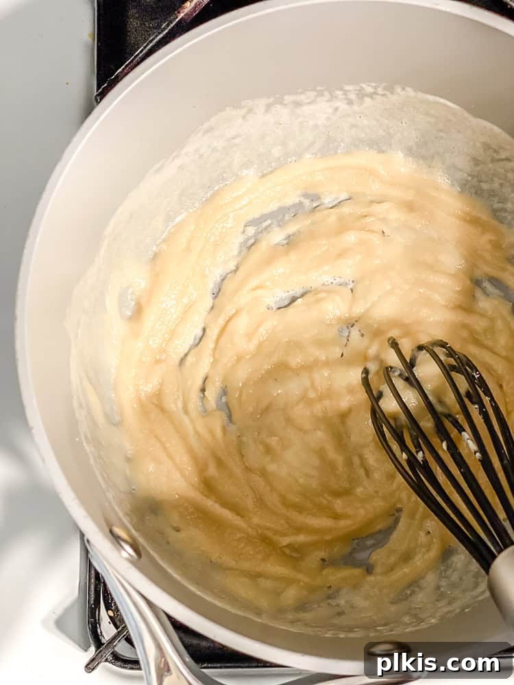Decadent Dairy-Free Scalloped Potatoes 5 A whisk vigorously mixing a golden-brown roux in a large grey pot, indicating the start of the creamy sauce preparation.