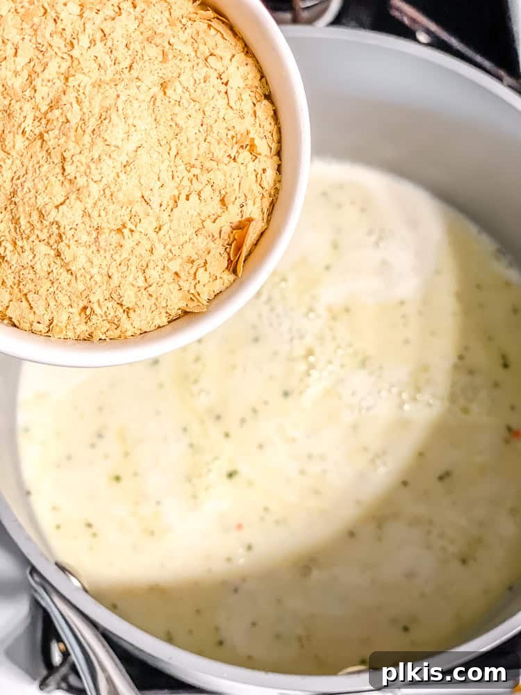 Decadent Dairy-Free Scalloped Potatoes 7 Nutritional yeast being sprinkled into a creamy sauce in a pot, adding a cheesy flavor.